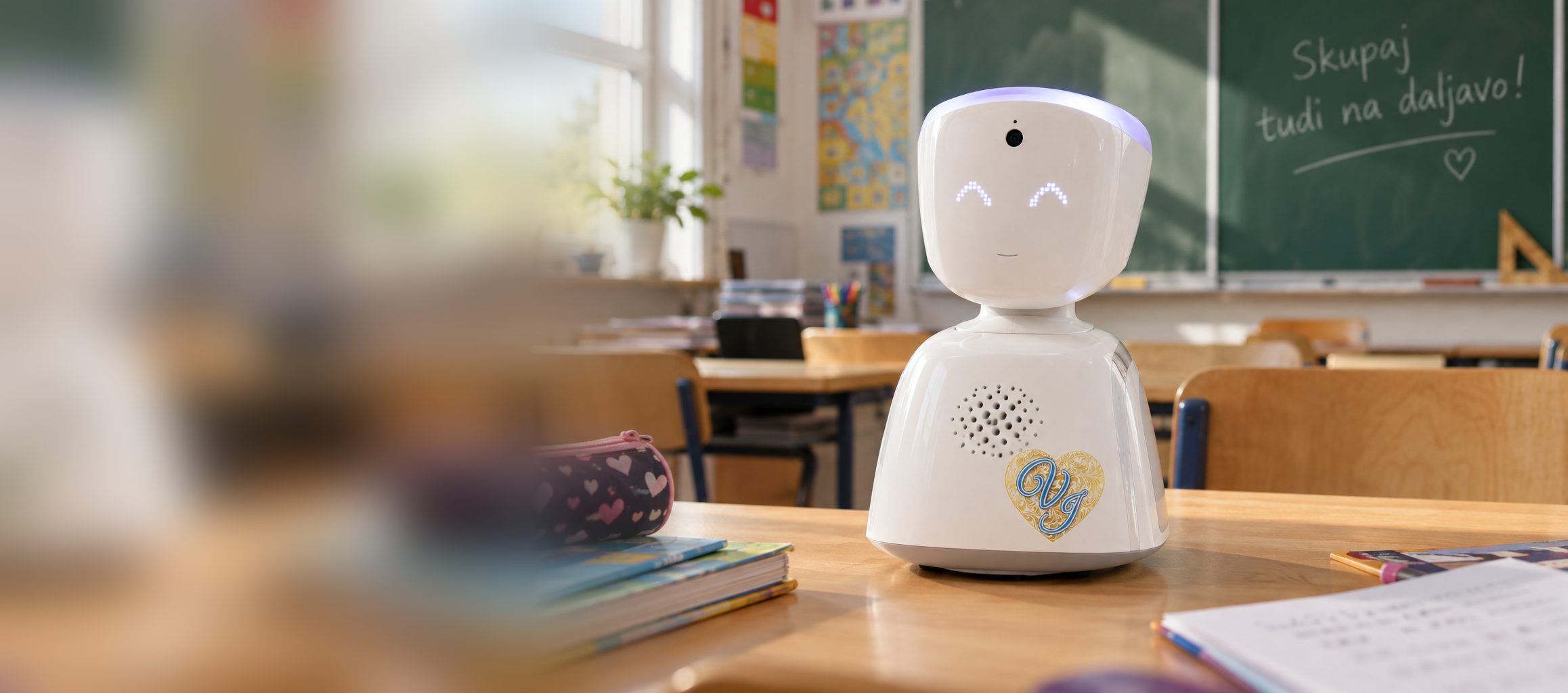 Robot AV1 s srcem Društva Viljem Julijan na šolski klopi pred tablo z napisom »Skupaj tudi na daljavo!«